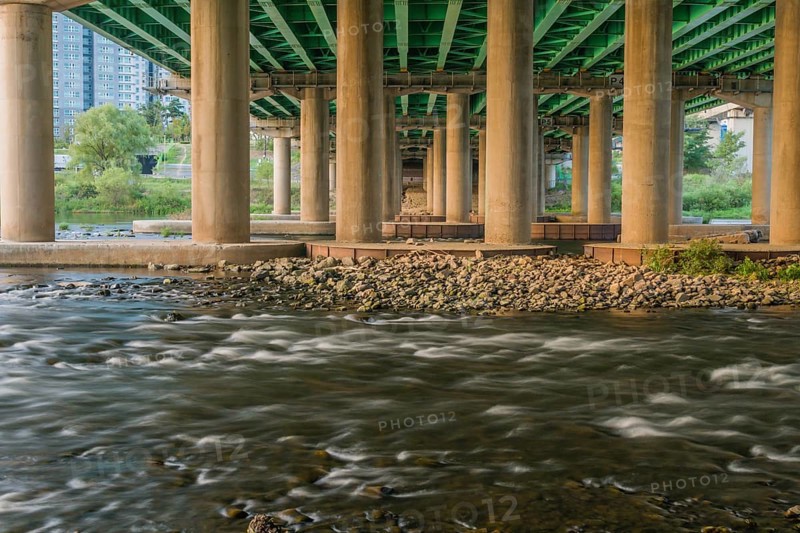 Long exposure shot of a river flowing under a green bridge with columns, in South Korea