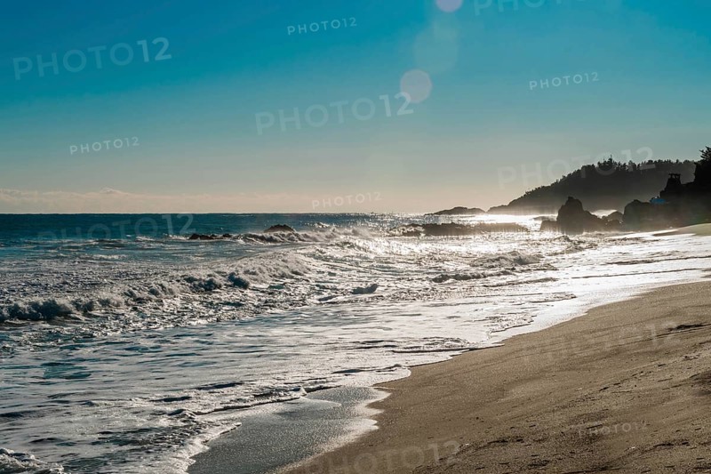 Rugged seascape with waves under bright morning sun crash onto beach and rocks under a beautiful blue sky, in South Korea