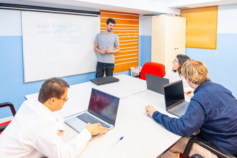 People with special needs attending a IT class using laptop while teacher explain using white board