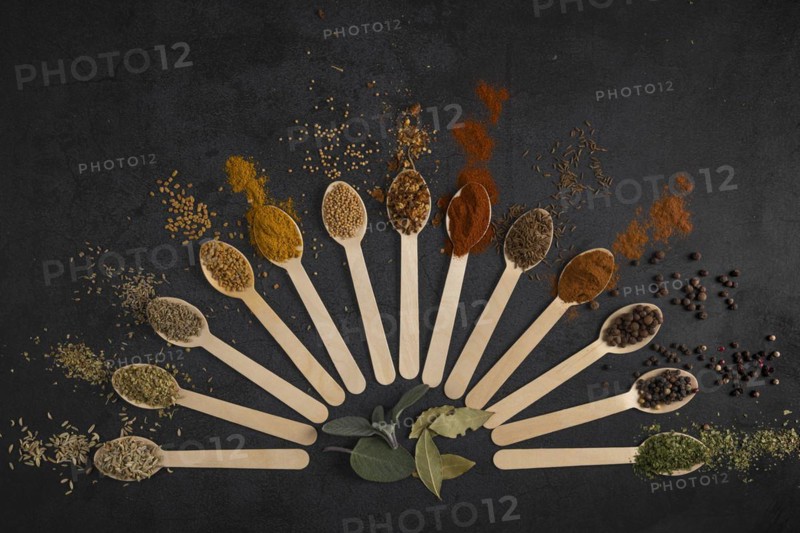 Colourful spices arranged in fan-shaped spoons on a dark background