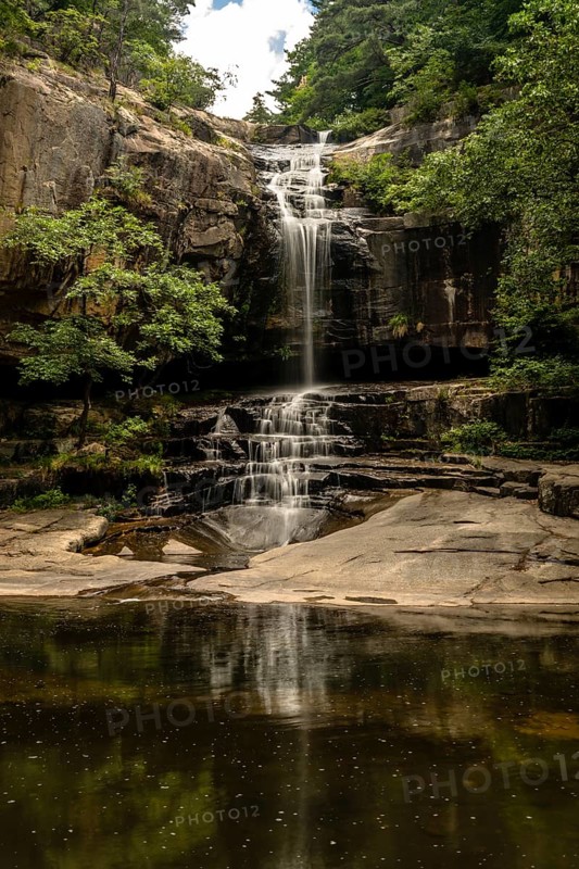 Gentle waterfall with its reflection visible in the clear, still water below, encased by forest, in South Korea