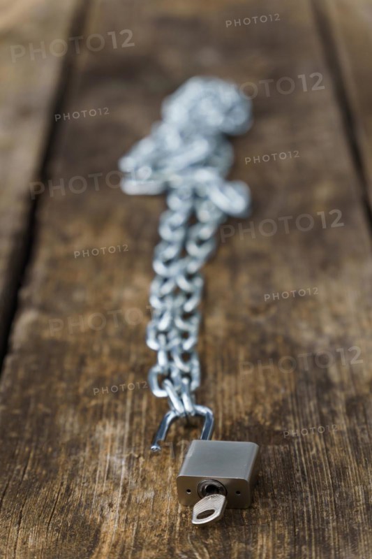 Shiny chain with padlock unlocked on a wooden table in a park with a selective focus