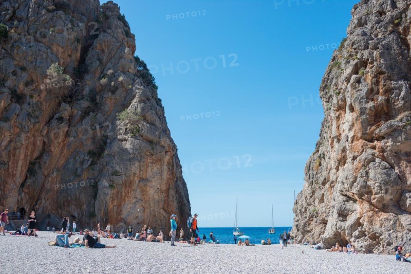 Torrent de Pareis, people relaxing on a popular tourist beach of pebbles framed by high cliffs, sight, cliffs, calm blue sea under a blue cloudless sky with anchored sailboats, yachts, sea, Mediterranean, Serra de Tramuntana gorge, Mediterranean Sea, Majorca Island, Spain, Europe