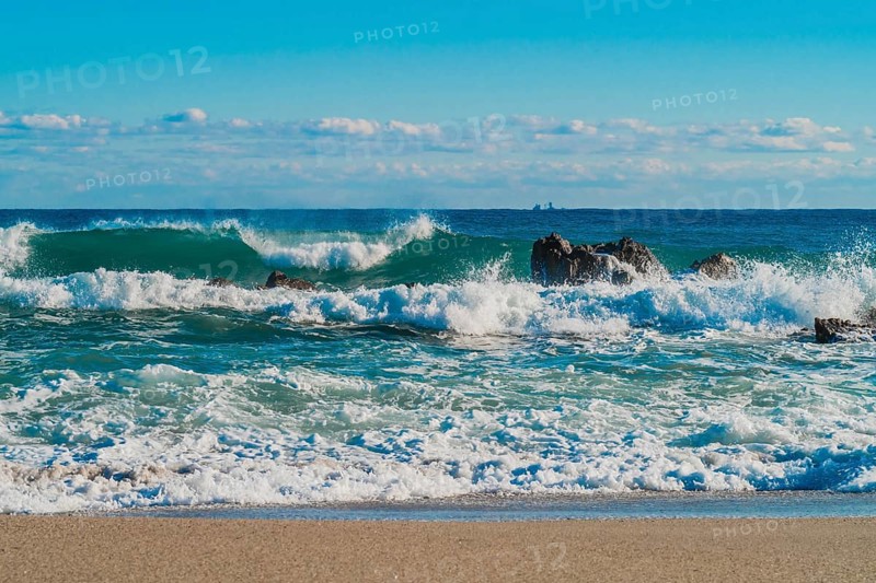 Foamy waves break on rocks with a clear horizon beyond under a deep blue sea, in South Korea