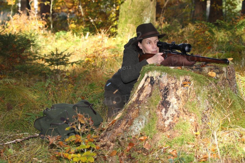 Huntress aims rifle with scope in colourful autumn forest, Allgaeu, Bavaria, Germany, Europe