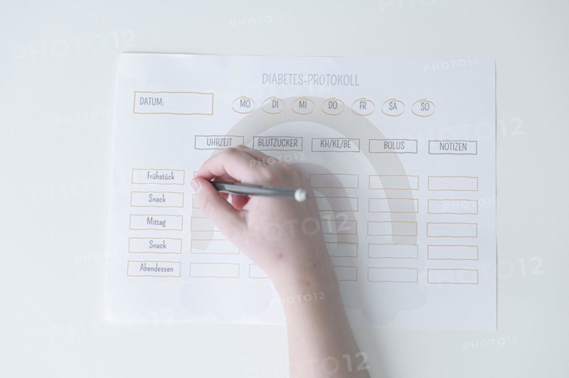 Diabetes log, daily log of food and insulin administration, food log, hand of a child holding a pen and appearing to fill in the log, the paper lies on a white table, Ruhr area, Germany, Europe