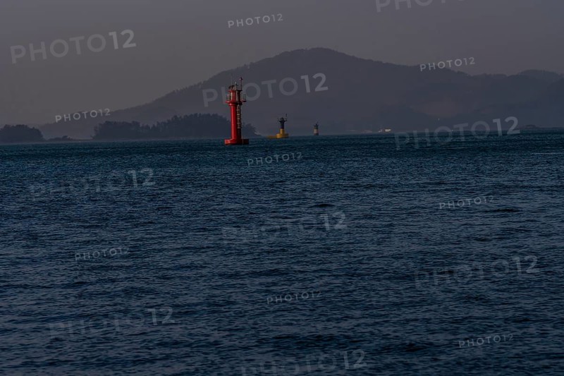 Three small light houses in a harbor with small mountains shrouded in fog and mist in the background in Namhae South Korea