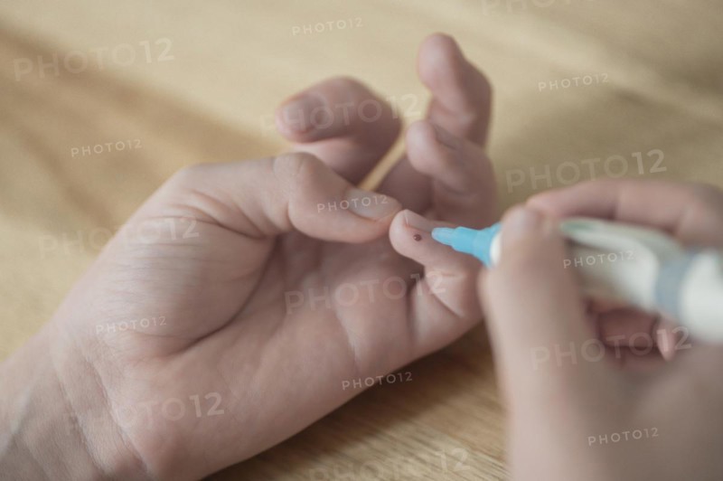On the left a child's hand with a drop of blood on the little finger, in the right hand the child holds the lancet, lancing device, has just pricked himself, wooden table as background, blood glucose measurement, diabetes treatment, glucose measurement, Ruhr area, Germany, Europe