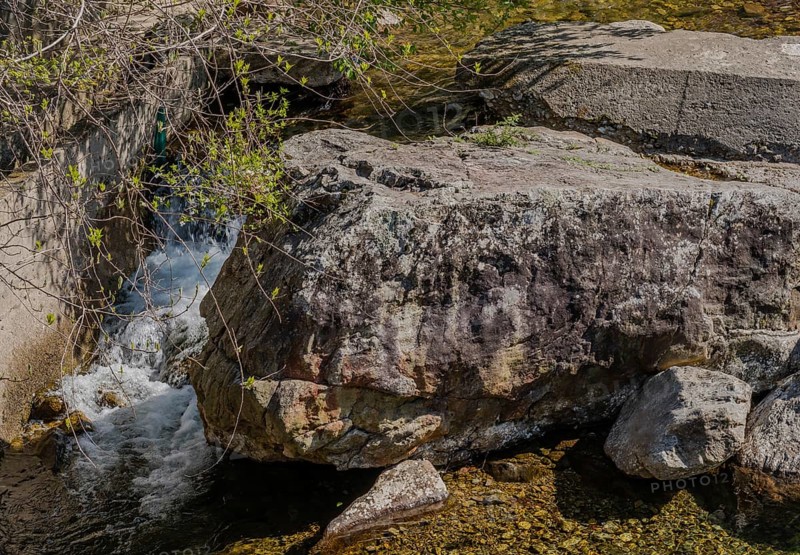 Water cascades down beside a large shaded rock, in South Korea