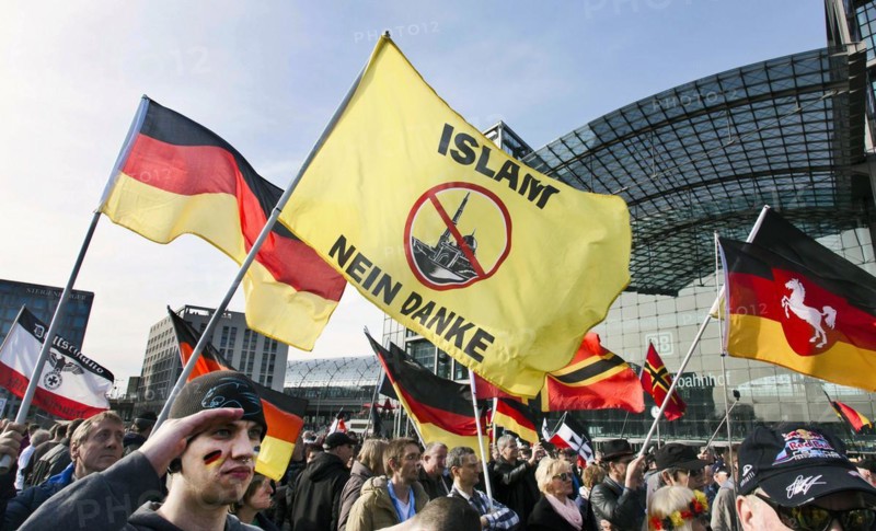 A participant in the Merkel muss weg demonstration holds a flag with the inscription Islam nein Danke . Demonstration by right-wing populist and right-wing extremist participants, including supporters of the NPD, Pegida, Reichsbuerger, hooligans, Landsmannschaften and Identitarians, Berlin, 4 March 2017