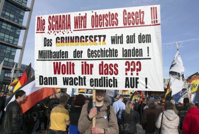 A participant in the Merkel muss weg demonstration holds a poster with the inscription Die Scharia wird oberstes Gesetz. Demonstration by right-wing populist and far-right participants, including supporters of the NPD, Pegida, Reichsbuerger, hooligans, Landsmannschaften and Identitarians, Berlin, 4 March 2017