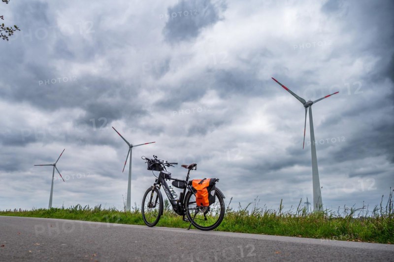 A parked bicycle at the roadside with wind turbines in the background under a cloudy sky, Leer, East Frisia, Lower Saxony