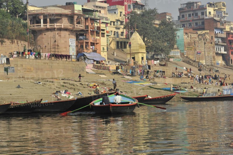 Boats at the edge of a river with people walking along the bank, Varanasi, Uttar Pradesh, India, Asia