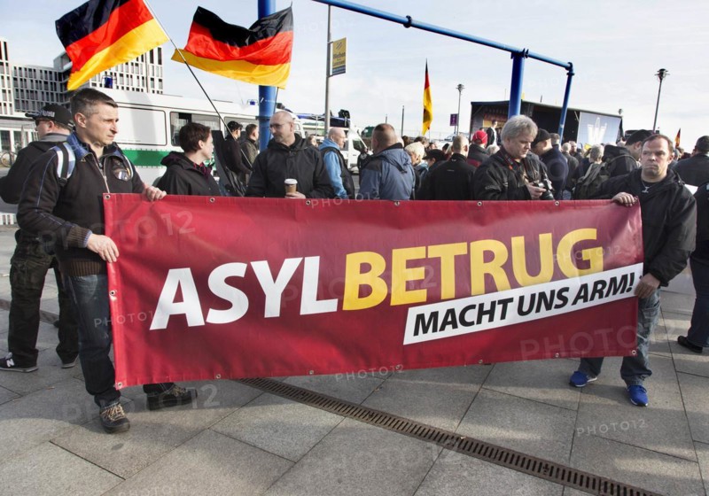 Participants in the Merkel muss weg demonstration hold a sign reading Asylum fraud makes us poor. Demonstration by right-wing populist and right-wing extremist participants, including supporters of the NPD, Pegida, Reichsbuerger, hooligans, Landsmannschaften and Identitarians, Berlin, 4 March 2017