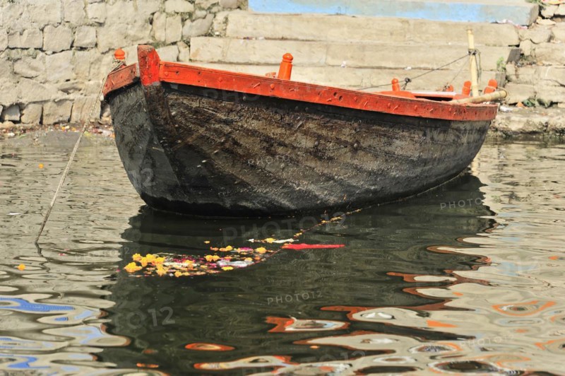 A single boat floats with a flower offering on the calm waters of a river in India, Varanasi, Uttar Pradesh, India, Asia