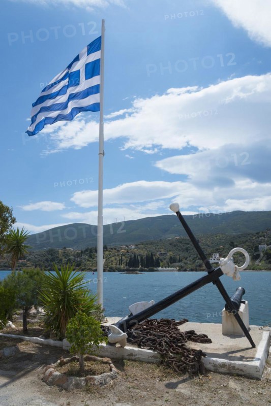 Greek flag flying next to a large anchor and cannon overlooking the sea and coastal landscape, Poros, Poros Island, Saronic Islands, Peloponnese, Greece, Europe