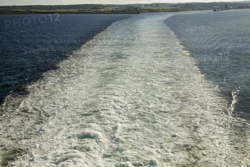 Large wake of ship at sea leaving land behind in the distance