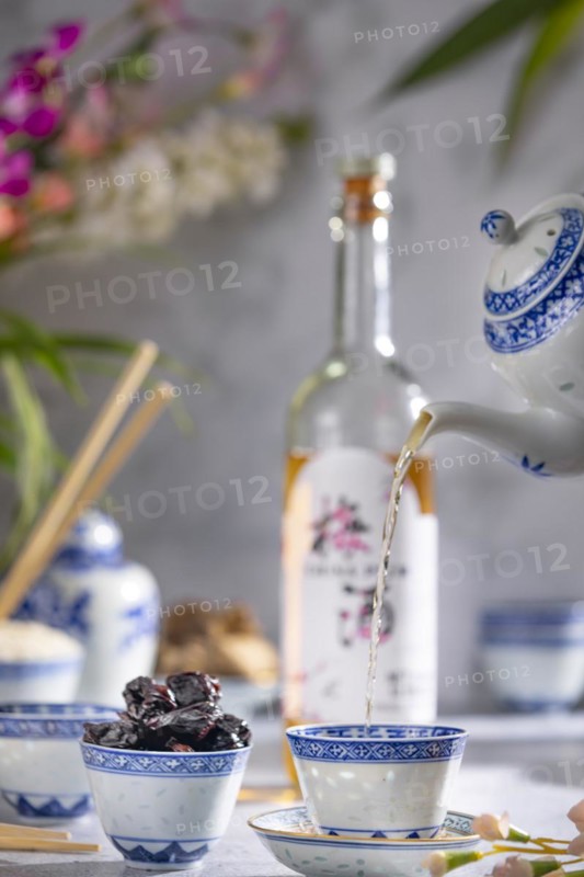 Pouring tea, Asian tea set with blue patterns, a bottle of China plum wine in the background, dried fruit