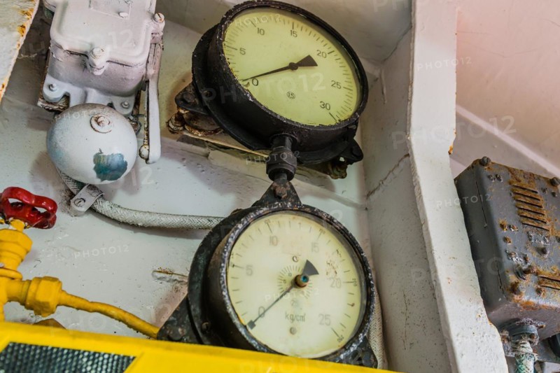 Old pressure gauges mounted above yellow and black striped ledge with valves and bell in background in Gangneung, South Korea, Asia