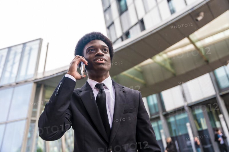 Low angle view close-up portrait of an elegant African young businessman working using phone outside a financial building