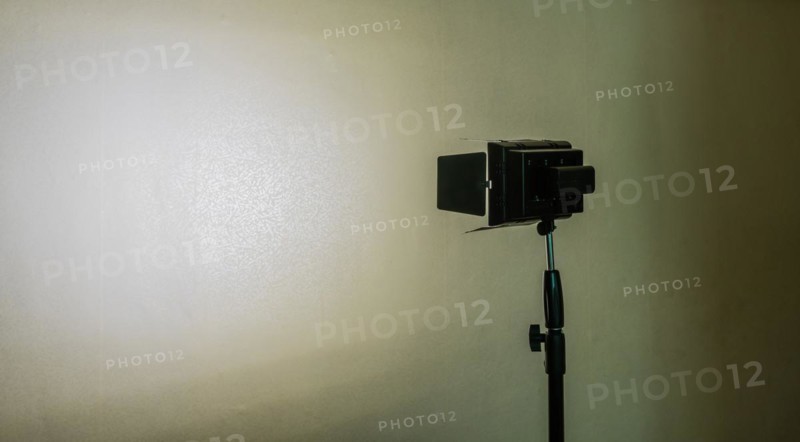 Continuous LED light mounted on tripod shinning on white patterned wall with deep shadows