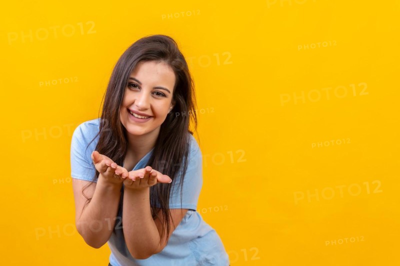 Studio portrait with yellow background of a smiling woman blowing a kiss with two hands