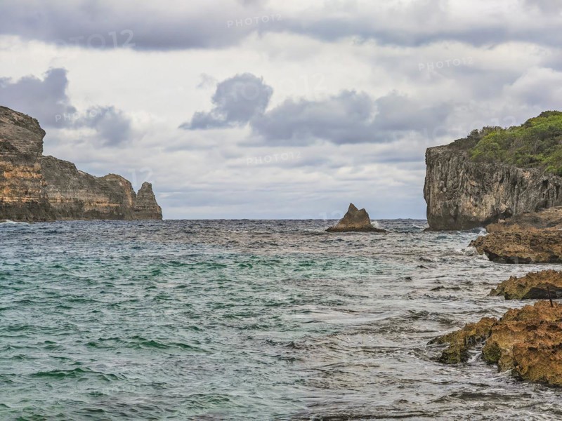 Rocky coast, long bay by the sea at sunset. Dangerous view of the Caribbean Sea. Tropical climate on a cloudy day in La Porte d'Enfer, Grande Terre, Guadeloupe, French Antilles, North America