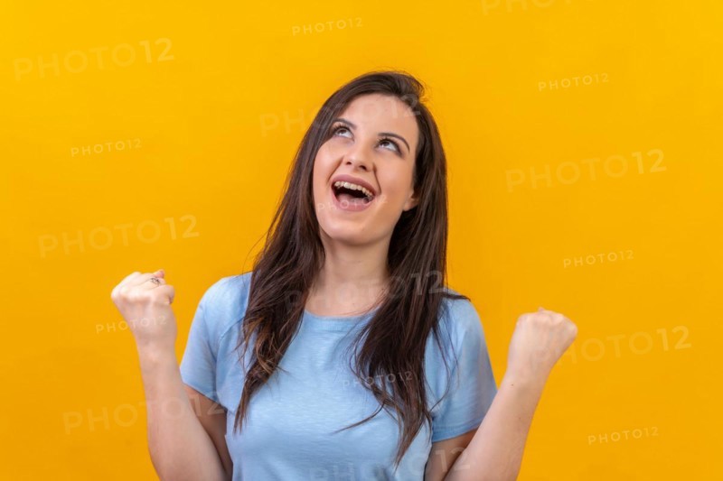 Studio portrait with yellow background of a woman looking up and raising fist celebrating