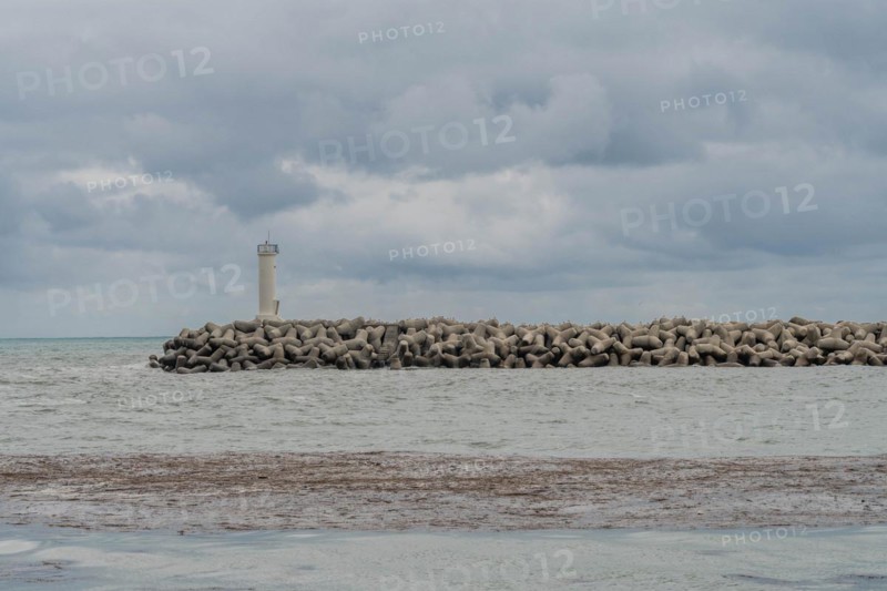 White lighthouse on a protective stone breakwater jutting out into a cloudy sea, in Ulsan, South Korea, Asia