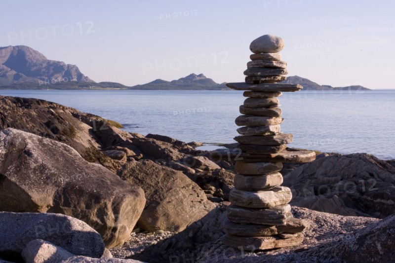 Balanced pile of stones on a quiet coastal landscape with a mountain panorama in the background Steinmann Lofoten Norway