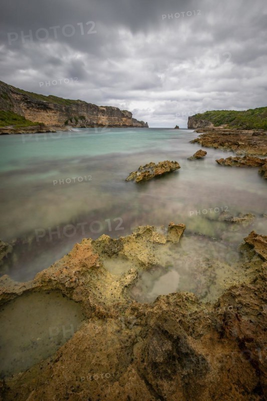Rocky coast, long bay by the sea at sunset. Dangerous view of the Caribbean Sea. Tropical climate on a cloudy day in La Porte d'Enfer, Grande Terre, Guadeloupe, French Antilles, North America
