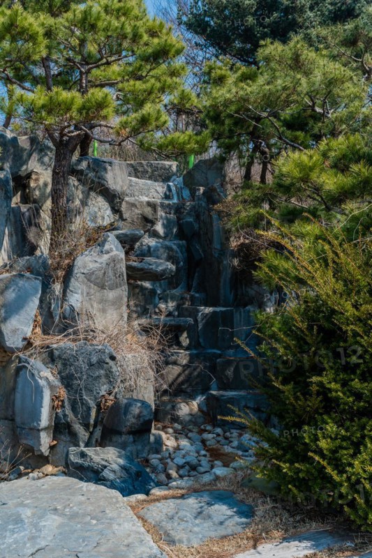 A small waterfall cascading down a rocky cliff surrounded by pine trees, in South Korea