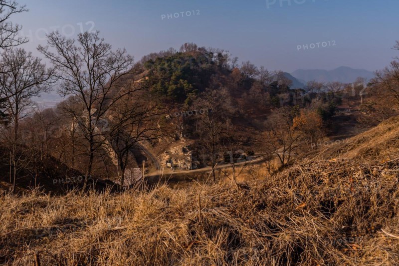 Section of mountain fortress wall behind leafless trees on top on winter morning with clear blue sky in background in Boeun, South Korea, Asia