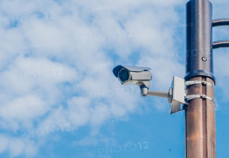 Surveillance camera mounted on metal light pole with blue sky and puffy white clouds in background in South Korea