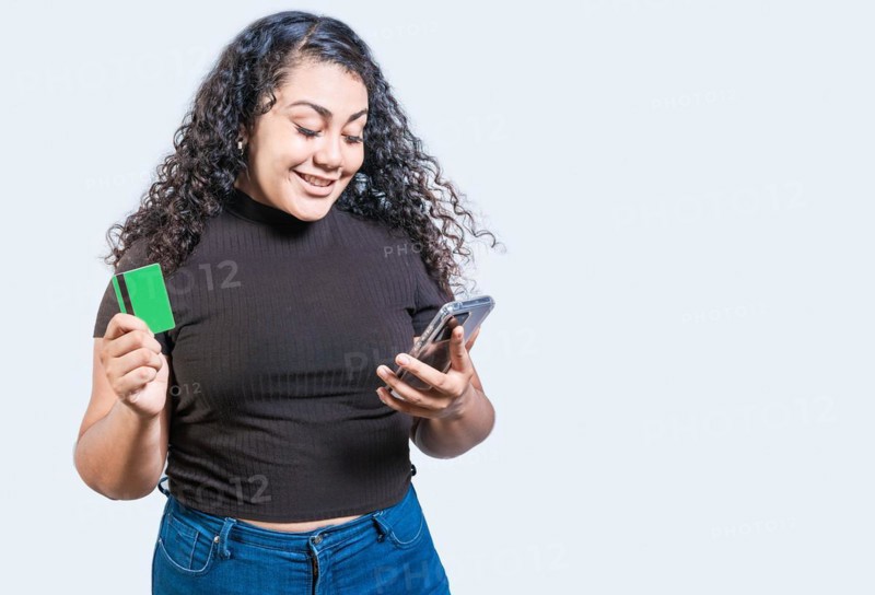 Happy girl holding credit card shopping online with phone isolated. Person making online purchases with cell phone and credit card isolated