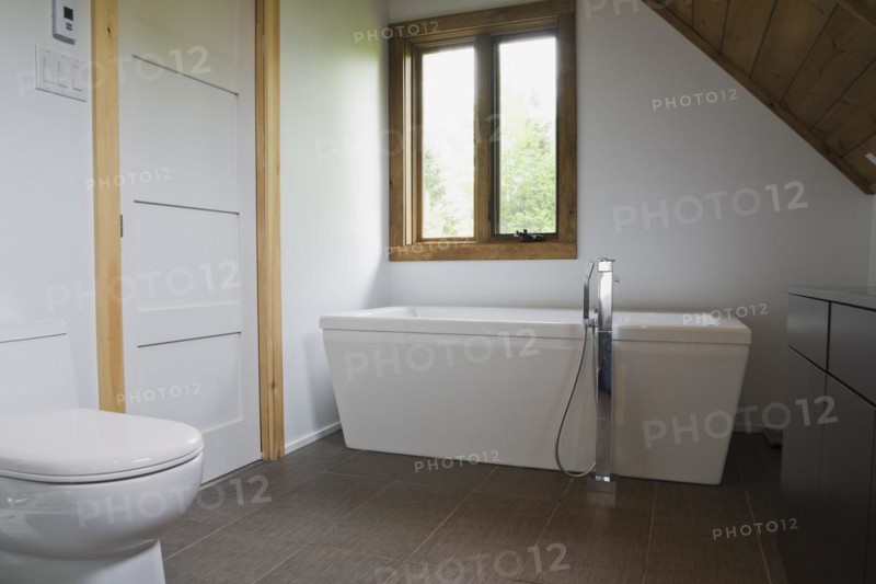 Main bathroom with grey ceramic tile floor and white porcelain toilet and freestanding bathtub on upstairs floor inside contemporary style log home, Quebec, Canada, North America