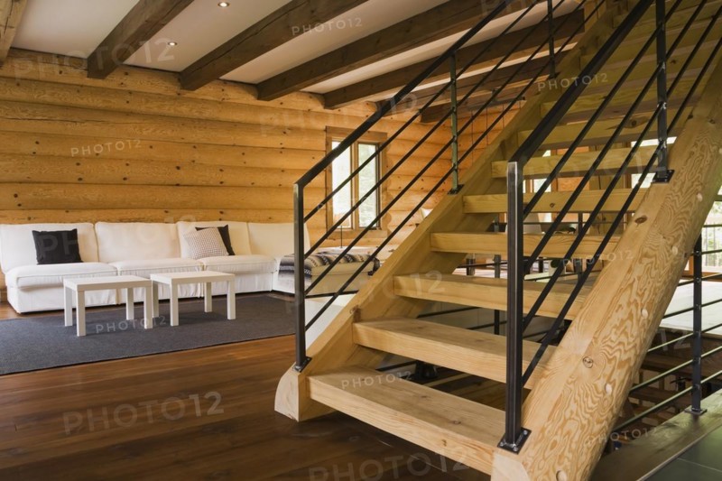 Wooden log stairs with black wrought iron railings and white cotton cloth upholstered sofas in living room inside contemporary style log home, Quebec, Canada, North America