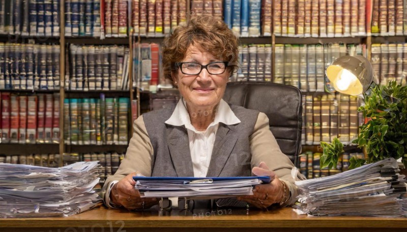 A smiling older woman in an office, surrounded by papers and a full bookshelf, symbolising bureaucracy, AI generated, AI generated