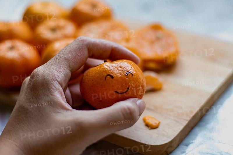A hand holding a clementine orange fruit with a smiling face drawn on it, concept of happiness, wellness and mental health wellbeing