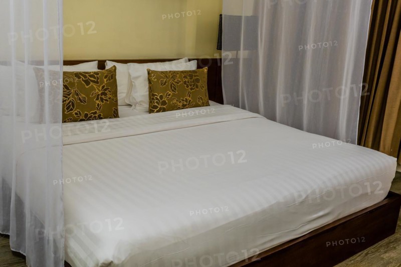 A neatly made bed with a mosquito net in a warmly lit bedroom, in Chiang Mai, Thailand, Asia