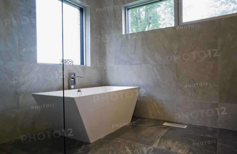 White freestanding vessel shaped bathtub in bathroom with grey ceramic tile floor and walls on ground floor inside modern cubist style home, Quebec, Canada. This image is property released. CUPR0269