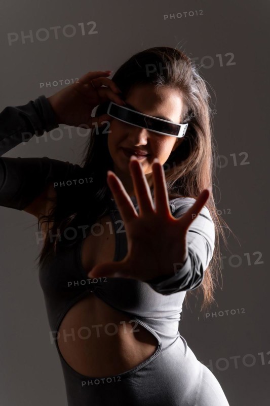 Studio portrait with grey background of a futuristic woman playing and gesturing using virtual reality mixed goggles