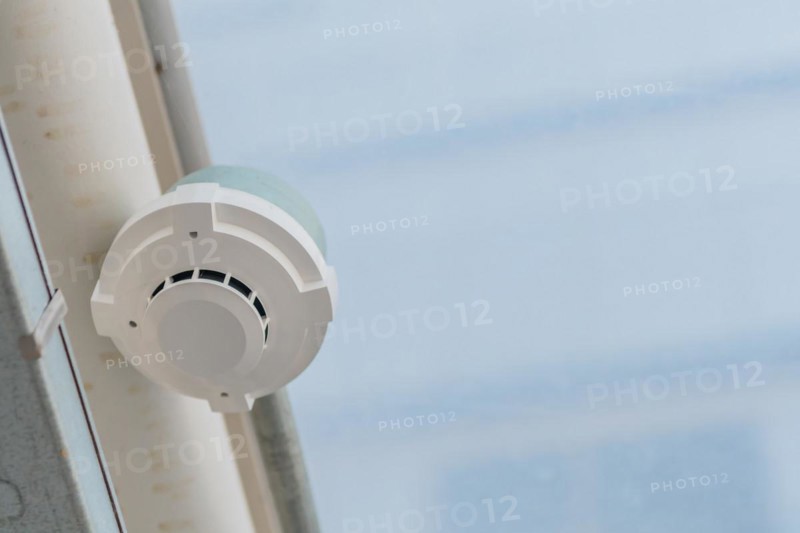 Electronic smoke detector on ceiling of enclosed pedestrian walkway with blurred plexiglass in South Korea