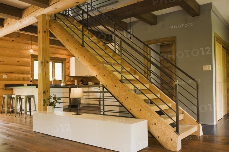 Kitchen with white wooden cabinets, metal bar stools and wooden log stairs with black wrought iron railings and long cabinet table inside contemporary style log home, Quebec, Canada, North America