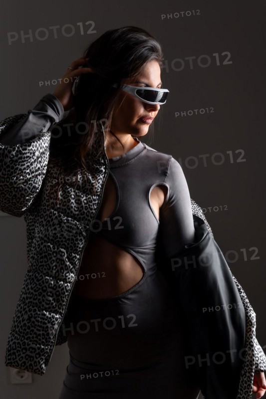 Vertical studio portrait with grey background of a futuristic woman in fashion clothes wearing intelligent goggles
