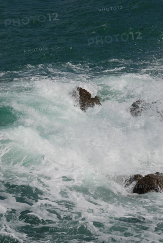 Turbulent waves crash against rocks, creating sea foam in the aquamarine ocean