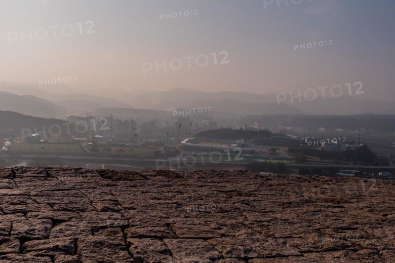 Top of mountain fortress wall made of flat stones with rural community under hazy sky in background in Boeun, South Korea, Asia