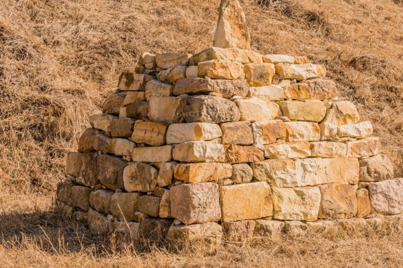 Closeup of pyramid shaped rock structure in field of brown grass at foot of hillside in Boeun, South Korea, Asia
