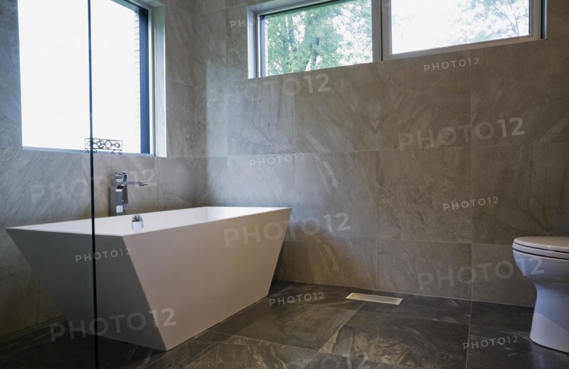 White freestanding vessel shaped bathtub in bathroom with grey ceramic tile floor and walls on ground floor inside modern cubist style home, Quebec, Canada, North America