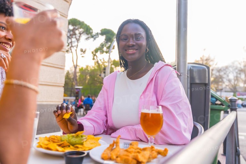 Smiling african young woman eating nachos with friends in an outdoor restaurant